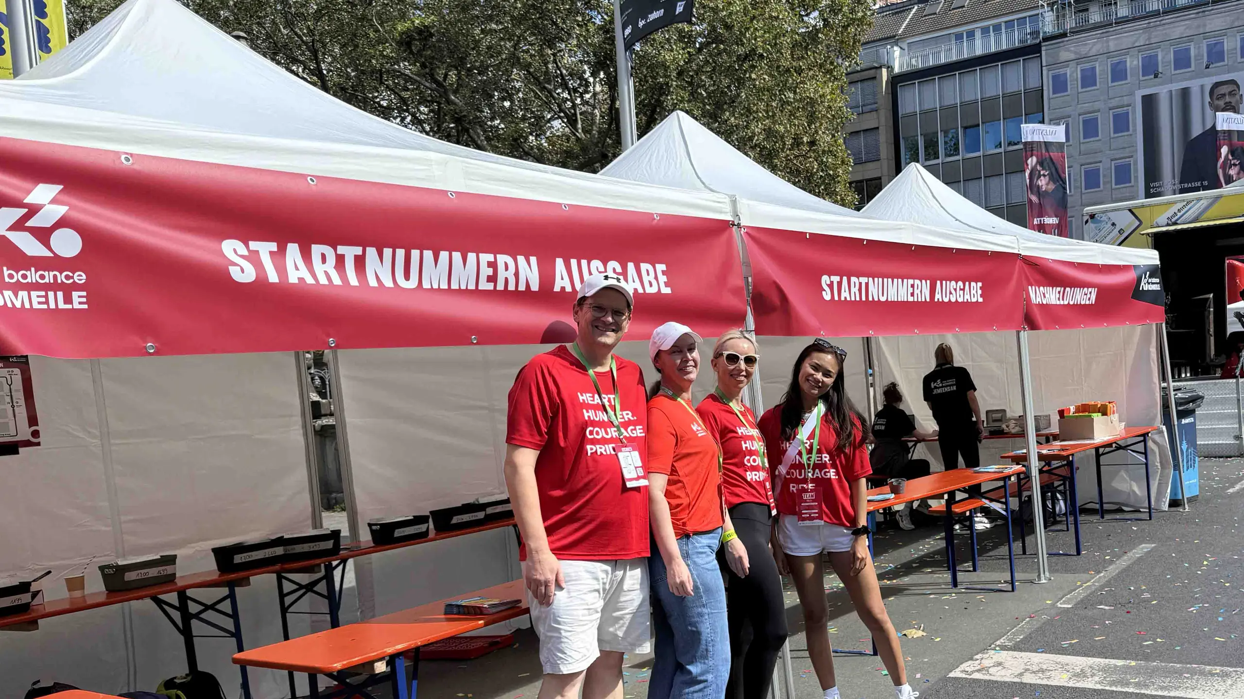 Volunteers in red shirts pose in front of race registration tents on a city street.