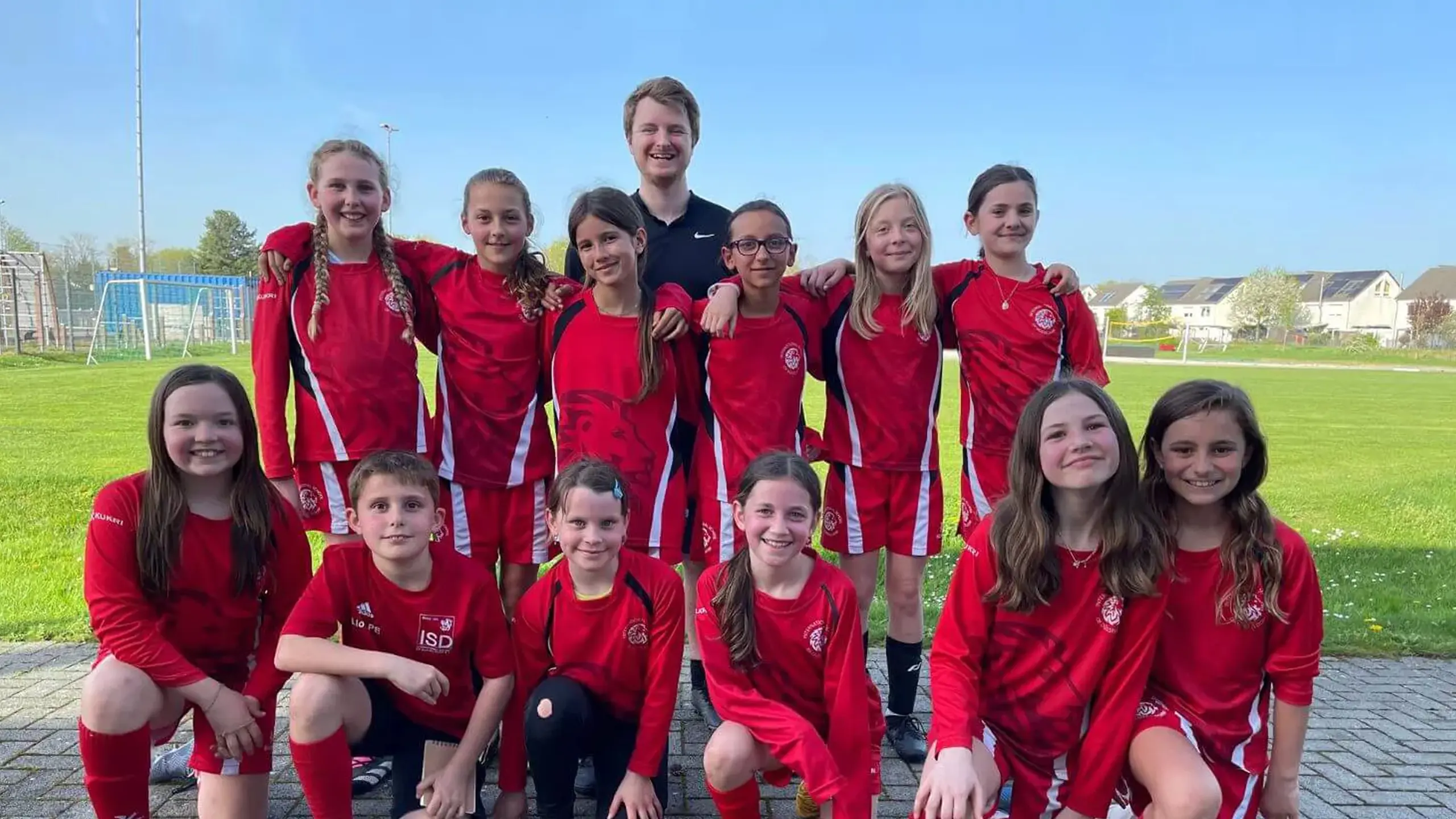 Young students with their coach posing for a group photo after a football game on a sports field at ISD.